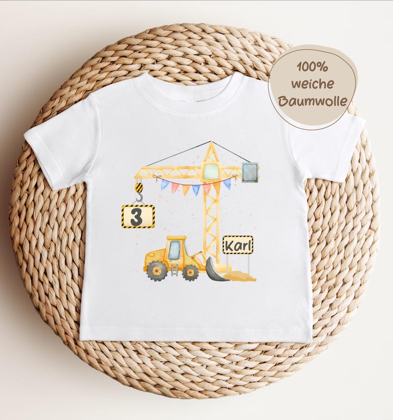 May include: A white short-sleeve t-shirt featuring a watercolor illustration of a yellow construction crane and a yellow bulldozer. The design includes a sign with the number 3, a sign with the name Karl, and colorful bunting flags.
