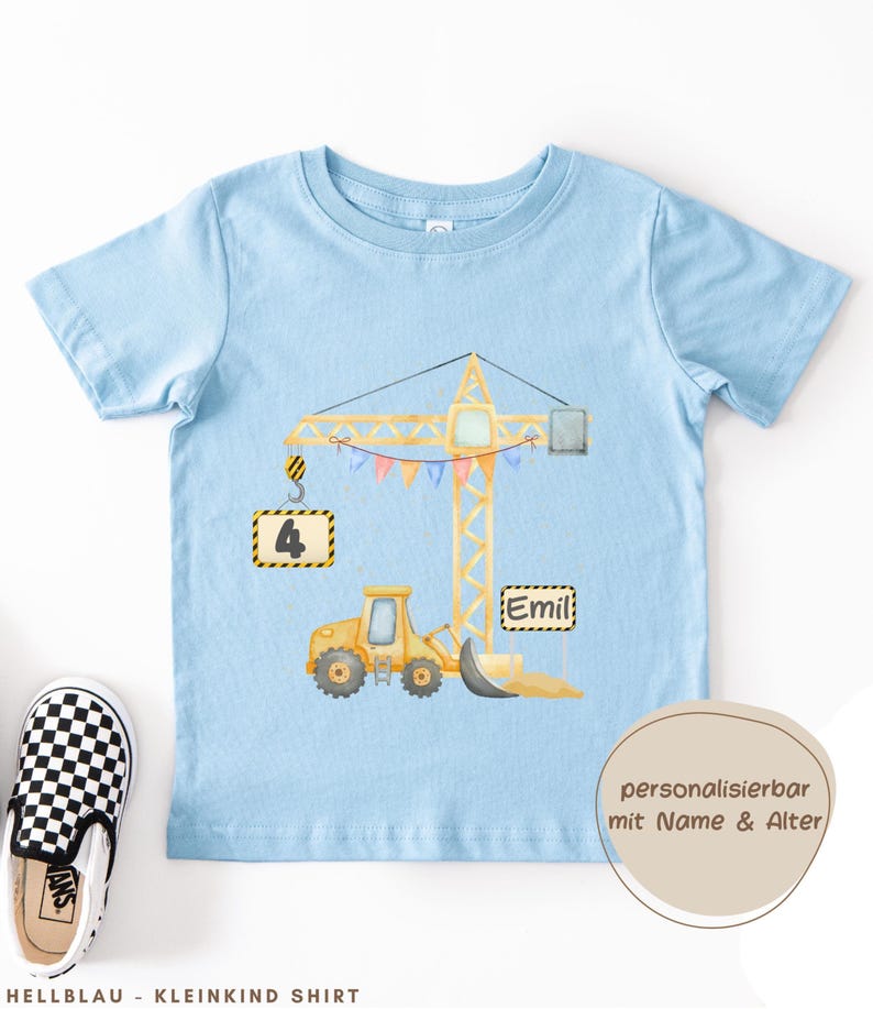 May include: A light blue short-sleeve t-shirt featuring a yellow construction crane graphic with a hanging sign displaying the number 4 and a second sign with the name Emil, decorated with colorful bunting flags and a yellow bulldozer.