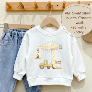 May include: A white long-sleeve sweatshirt featuring a watercolor illustration of a yellow construction crane and a bulldozer. The crane holds a sign with the number 3, and a sign with the name Emil is near the bulldozer. Text reads: Als Sweatshirt in den Farben: -wei&szlig; -schwarz -navy.