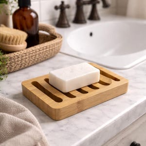 May include: A rectangular bamboo soap dish with a white bar of soap. The dish has several parallel slots for drainage. The bathroom setting includes a sink, faucet, and a brown bottle of soap.