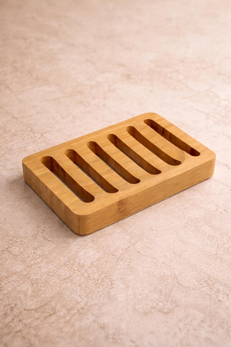May include: A rectangular bamboo soap dish with seven parallel slots. The dish is made of light brown bamboo and has a simple, minimalist design. The slots allow for drainage, extending the life of the soap. The dish is suitable for the bathroom or kitchen.