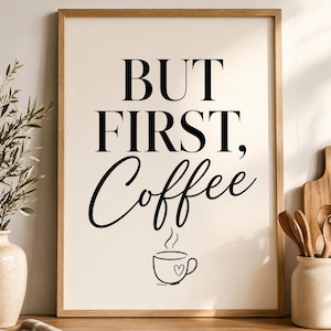 May include: Framed wall art with the text "BUT FIRST, Coffee" in black lettering. The word "Coffee" is in a cursive font, and a coffee cup with a heart is below the text. The frame is a light brown color.