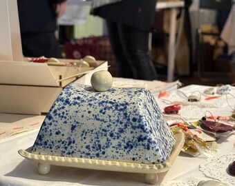 Manteigueira artesanal de cerâmica com detalhes salpicados em azul e branco.