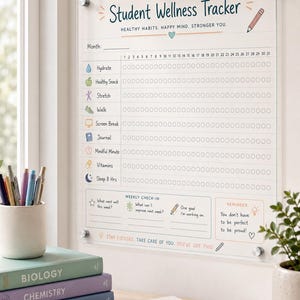 May include: A clear acrylic wall-mounted Student Wellness Tracker board featuring a monthly habit grid with icons for hydration, snacks, stretching, walking, screen breaks, journaling, mindfulness, vitamins, and sleep, plus a weekly check-in section.