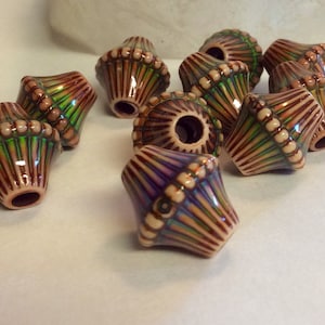May include: A group of eight brown and cream ceramic beads with green and purple iridescent accents. The beads are shaped like a cone with a rounded top and a hole in the bottom.