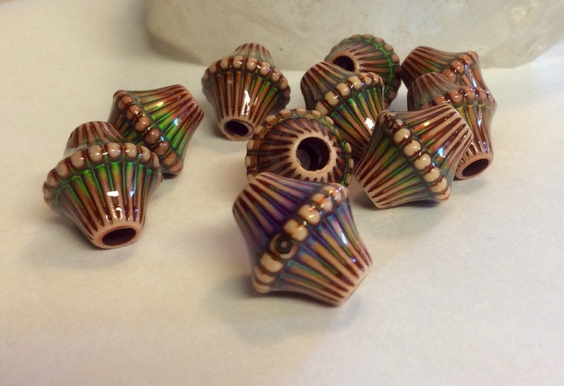 May include: A group of eight brown and cream ceramic beads with green and purple iridescent accents. The beads are shaped like a cone with a rounded top and a hole in the bottom.