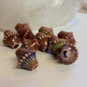 May include: A group of ten brown and white ceramic beads with a geometric design. The beads have a shiny iridescent glaze.