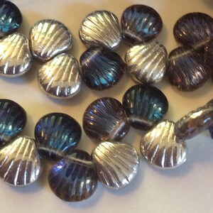 May include: A strand of iridescent glass beads in the shape of seashells. The beads are a mix of silver and blue.