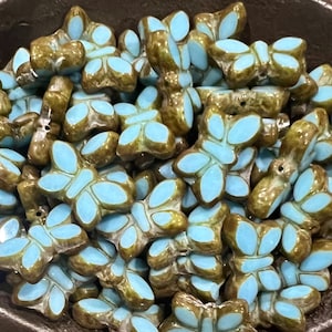 May include: A collection of butterfly-shaped beads. The beads have a light blue center and a brown, textured exterior. The beads are clustered together, filling the frame.