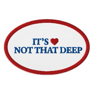 Puede incluir: Parche bordado ovalado con borde rojo y centro blanco. El texto "IT'S ♥ NOT THAT DEEP" está bordado en azul, con un símbolo de corazón rojo. El parche está diseñado para ropa o accesorios.