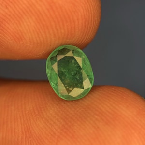May include: A loose oval-cut emerald gemstone with a vibrant green hue and multifaceted surface. The stone displays natural internal inclusions and a polished finish, showcasing a classic faceted design that reflects light across its surface.