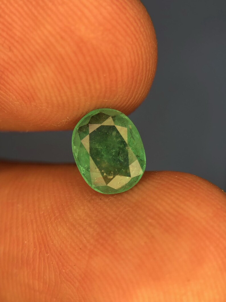 May include: A loose oval-cut emerald gemstone with a vibrant green hue and multifaceted surface. The stone displays natural internal inclusions and a polished finish, showcasing a classic faceted design that reflects light across its surface.