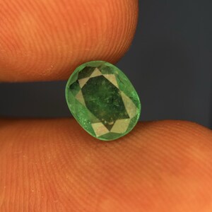 May include: An oval-cut, vibrant green gemstone featuring a faceted surface that reflects light. The stone displays a translucent quality with visible internal inclusions and a polished finish, showcasing a classic, symmetrical geometric cut.