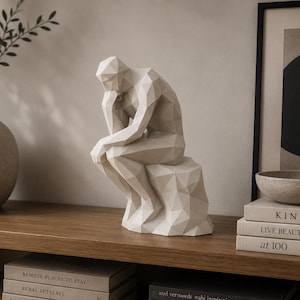 May include: A white, geometric, low-poly sculpture of a seated figure in a contemplative pose, resting its chin on one hand. The figure is composed of sharp, angular facets, creating a modern, faceted appearance that mimics the classic thinker pose.