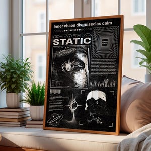May include: A framed black and white art print with the text "Inner chaos disguised as calm" and "STATIC". The artwork features an eye, geometric shapes, and a skull. The frame is made of wood and is displayed near a window with plants.