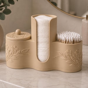 May include: A beige bathroom organiser featuring a central vertical slot for cotton rounds, a lidded compartment on the left, and an open section on the right for cotton swabs. The exterior is decorated with embossed floral patterns and vines.