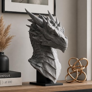 Könnte beinhalten: Eine graue Drachenkopfskulptur mit detaillierten Schuppen, spitzen Hörnern und einer strukturierten Oberfläche. Die Büste ist auf einem schwarzen rechteckigen Sockel montiert und zeigt das Profil mit einer markanten Schnauze und definierten Zügen.