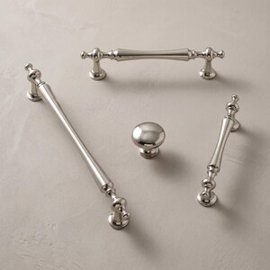 May include: A collection of polished silver-toned metal hardware including two long drawer pulls, one shorter drawer pull, and one round cabinet knob. Each piece features a smooth, reflective finish with decorative, tiered pedestal bases.