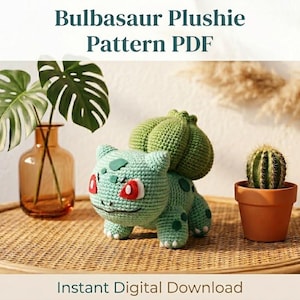 May include: A crocheted Bulbasaur plushie with a green body, red eyes, and a bulb on its back. The image also features a vase with green leaves, a small cactus in a terracotta pot, and the text "Bulbasaur Plushie Pattern PDF".