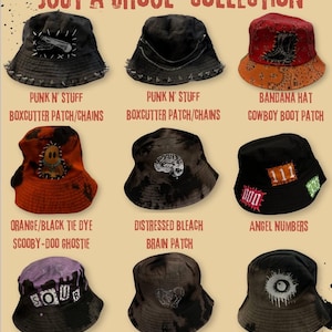 Op de afbeelding: Een collectie emmerhoeden met diverse ontwerpen. De hoeden hebben patches, kettingen en tie-dye patronen. Sommige hoeden hebben tekst met "JUST A GHOUL" en andere tekst. Kleuren zijn zwart, oranje, rood en paars.