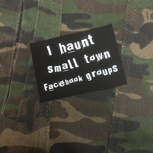 May include: A camouflage-patterned jacket with a black rectangular patch. The patch features white text that reads "I haunt small town Facebook groups."
