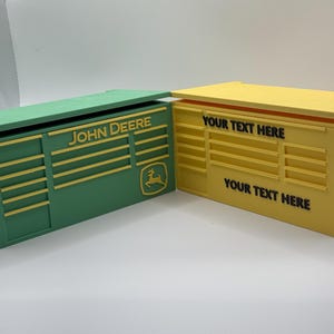 May include: Two rectangular boxes, one green and one yellow, with hinged lids. The green box features the text "JOHN DEERE" and a logo. The yellow box has the text "YOUR TEXT HERE". Both boxes have a slotted design.