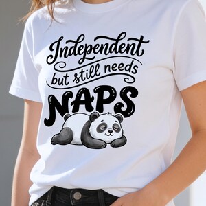 Może przedstawiać: Biała koszulka z napisem "Independent but still needs NAPS" w czarnym skrypcie. Poniżej tekstu leży czarno-biały rysunkowy miś panda. Koszulka ma okrągły dekolt.