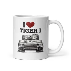 Könnte beinhalten: Weiße Keramiktasse mit schwarzer und roter Grafik. Das Design zeigt eine detaillierte Illustration eines Tiger I-Panzers mit dem Text "I ❤️ TIGER I" darüber. Die Tasse hat einen Standardgriff.