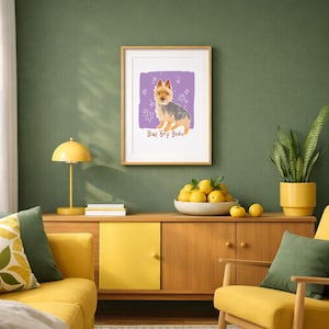 May include: A framed wall art print featuring a tan and grey terrier dog illustration on a purple background with white flower doodles and the text Bad Boy Bean written in brown letters below the dog, displayed in a light wood frame.