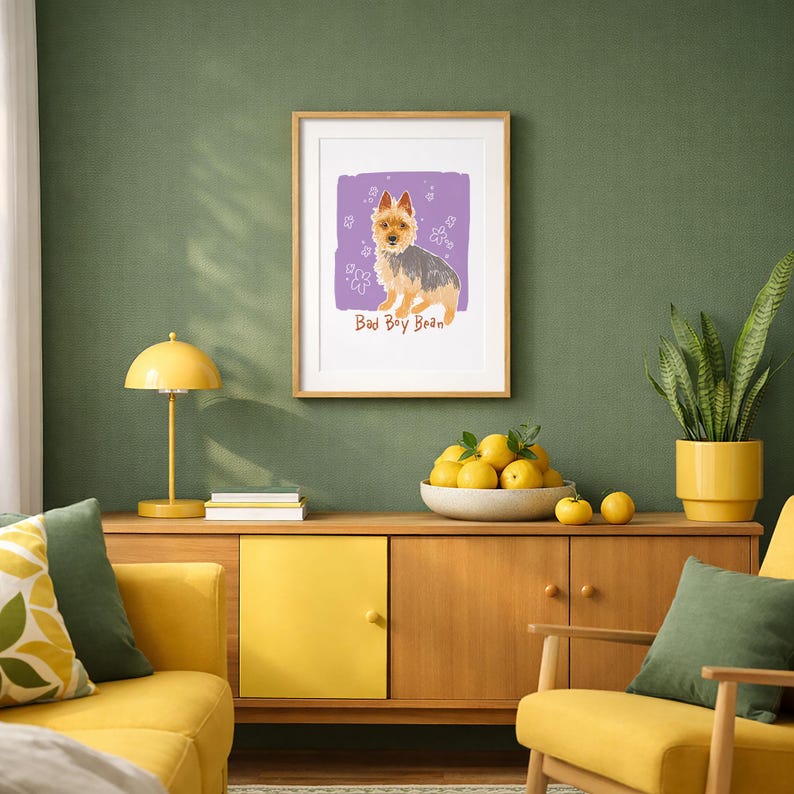 May include: A framed wall art print featuring a tan and grey terrier dog illustration on a purple background with white flower doodles and the text Bad Boy Bean written in brown letters below the dog, displayed in a light wood frame.