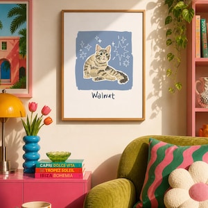 May include: A framed wall art print featuring a brown tabby cat illustration centred on a blue square background with white star accents. The name Walnut is printed in dark blue text below the cat. The print is enclosed in a thin wooden frame.