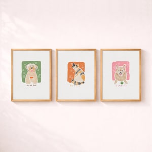 May include: Three framed wall art prints featuring illustrations of pets. The left print shows a tan dog on a green background with the text MY BOY BORI. The centre print shows a calico cat on an orange background with the text KITTY. The right print shows a tan dog with a ball on a pink background with the text I LOVE IT.