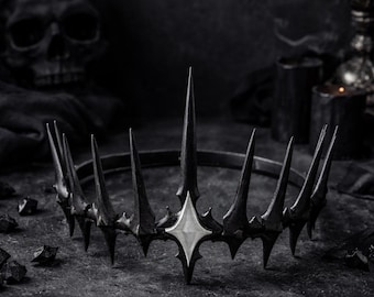 Könnte beinhalten: Eine gotische Krone mit dunklem, metallischem Finish. Die Krone hat mehrere scharfe, längliche Spitzen und ein zentrales, rautenförmiges Ornament. Das Design erinnert an dunkle Fantasie und Königtum.