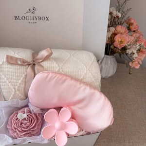 Puede incluir: Caja de regalo con una m&aacute;scara de ojos de sat&eacute;n rosa, una pinza para el pelo con forma de flor y una vela con forma de rosa. Tambi&eacute;n se incluye una manta color crema atada con una cinta. La caja tiene el texto "BLOCMYBOX SHOP".