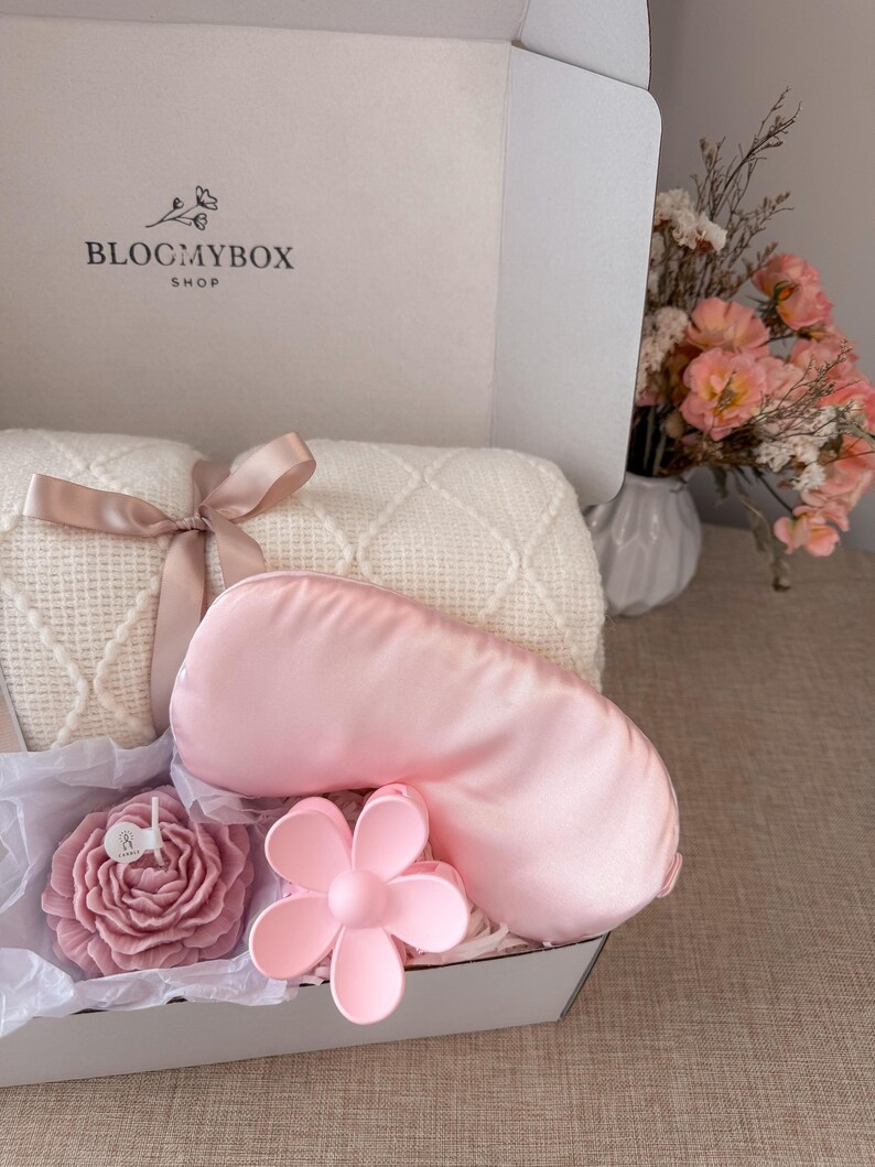 Puede incluir: Caja de regalo con una m&aacute;scara de ojos de sat&eacute;n rosa, una pinza para el pelo con forma de flor y una vela con forma de rosa. Tambi&eacute;n se incluye una manta color crema atada con una cinta. La caja tiene el texto "BLOCMYBOX SHOP".
