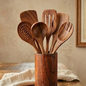 Può includere: Un set di sei utensili da cucina in legno marrone disposti in un portautensili cilindrico in legno. La collezione comprende una spatola forata, un cucchiaio pieno, un cucchiaio forato, una forchetta e due spatole piatte in legno.