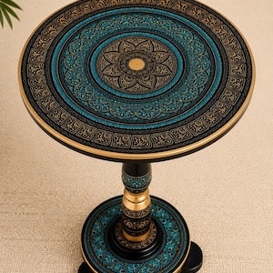 Peut inclure: Une table d'appoint ronde avec une base noire ornée de motifs complexes dorés et bleu sarcelle de style mandala. Le plateau présente un motif floral central entouré d'anneaux concentriques aux dessins géométriques détaillés sur un pied.
