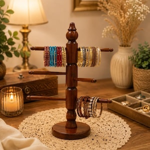 May include: A dark brown wooden jewelry stand with a central pillar and three horizontal arms. The top arm holds red, blue, and gold bangles. The bottom arm holds brown and gold textured bangles. The stand has a round base and a finial top.