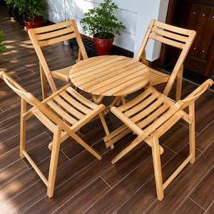 May include: A light brown wooden patio set consisting of a round slatted table and four matching folding chairs. The furniture features a natural wood grain finish with horizontal slats on the chair backs and seats, arranged in a circular formation.