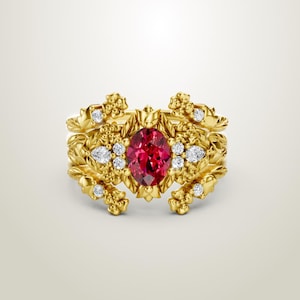 May include: A gold ring featuring an oval, ruby-red gemstone at the center, surrounded by smaller white gemstones and ornate floral detailing. The ring has a layered design with intricate leaf and flower patterns.