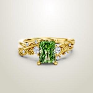 May include: A gold ring set featuring a vibrant green emerald-cut gemstone as the focal point. The ring is adorned with smaller, sparkling white diamonds and a delicate, vine-like design. The band is a warm gold color.