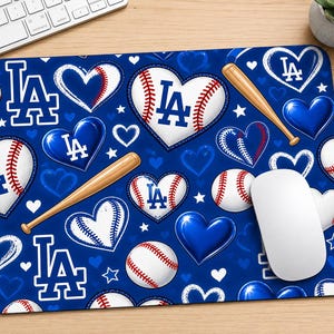 May include: A rectangular mouse pad featuring a blue background with a repeating pattern of white hearts, baseballs with red stitching, wooden baseball bats, and the blue LA logo. The design includes various heart shapes, some solid blue and some outlined.