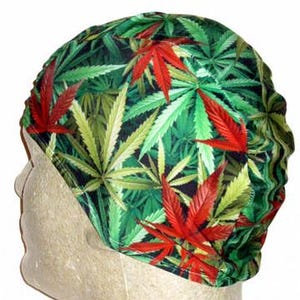 May include: A green, red, and yellow leaf-patterned head covering. The fabric features a repeating design of cannabis leaves in various shades of green, with accents of red and yellow. The head covering is worn on a mannequin head.