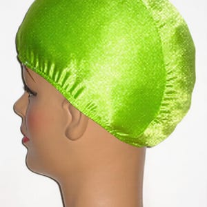 May include: A bright green satin cap, likely for hair protection or styling, is shown on a mannequin head. The cap is a vibrant, solid color, and the fabric has a slight sheen. The cap covers the top and back of the head.