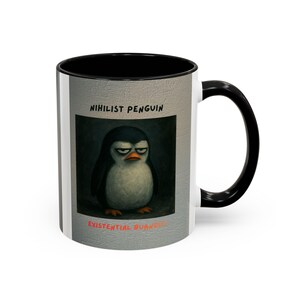 May include: A white ceramic coffee mug with a black interior and handle. The mug features a graphic of a grumpy penguin with the text "Nihilist Penguin" and "Existential Burnout".