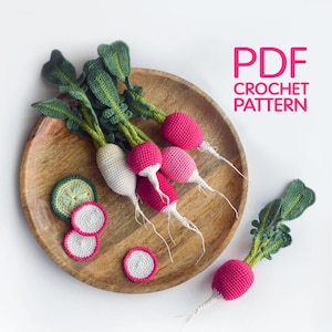 Op de afbeelding: Een houten bord toont gehaakte radijsjes met groene bladeren en witte wortels. De radijsjes zijn roze en wit, met gehaakte limoenschijfjes. De tekst "PDF CROCHET PATTERN" is roze.