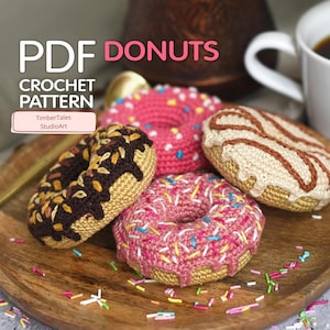 May include: Crocheted donuts in various colors, including pink, brown, and beige, with colorful sprinkles. The image includes text that reads "PDF DONUTS" and "CROCHET PATTERN" with the StudioArt logo. The donuts are arranged on a wooden tray.