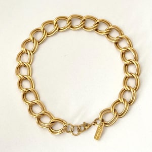 May include: A gold-toned chain link bracelet with a lobster clasp closure. The bracelet features a series of oval links, creating a bold and classic design. A small tag with the brand name "Monet" is attached near the clasp.