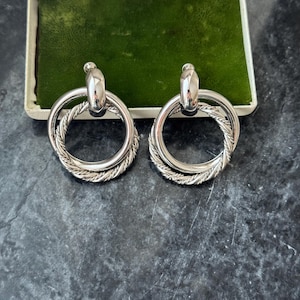 Peut inclure: Une tasse en céramique blanche avec une anse noire et le texte "But First, Coffee" en gras noir. La tasse est placée sur un fond flou. La tasse mesure environ 10 cm de hauteur.