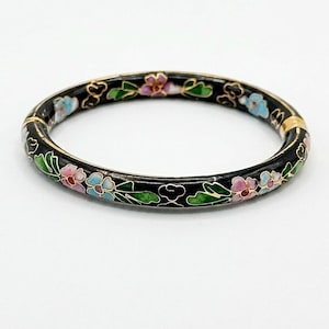 May include: A black metal bangle bracelet featuring a colourful cloisonné enamel floral pattern with pink, light blue, and green petals and leaves outlined in thin gold-tone wire. The circular bracelet has a hinged clasp mechanism on one side.